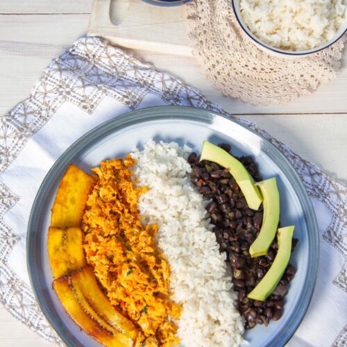 Un plato de pabellón de pescado con pisillo, arroz, caraotas, platano frito, y aguacate