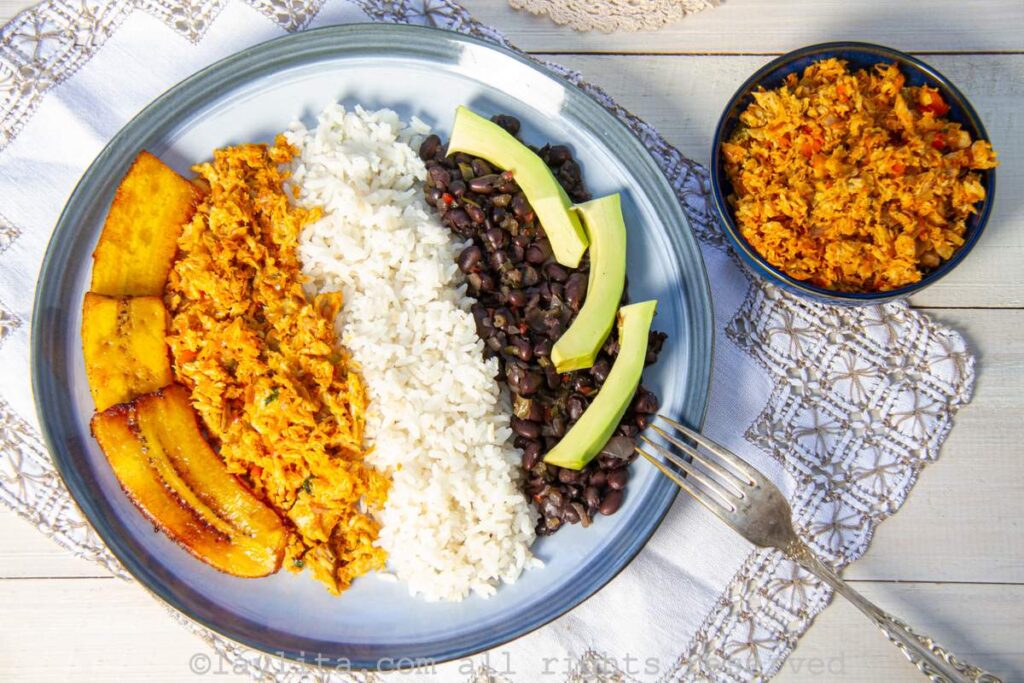 Un plato de pabellón de pescado con pisillo, arroz, caraotas, platano frito, y aguacate