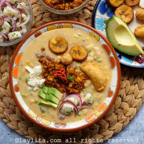 Un plato hondo lleno de fanesca ecuatoriana con guarniciones encima de la sopa y al lado