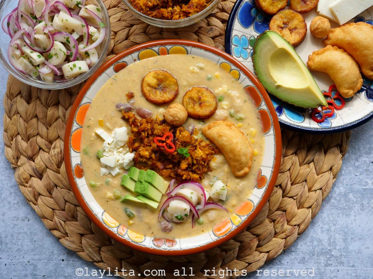 Un plato hondo lleno de fanesca ecuatoriana con guarniciones encima de la sopa y al lado