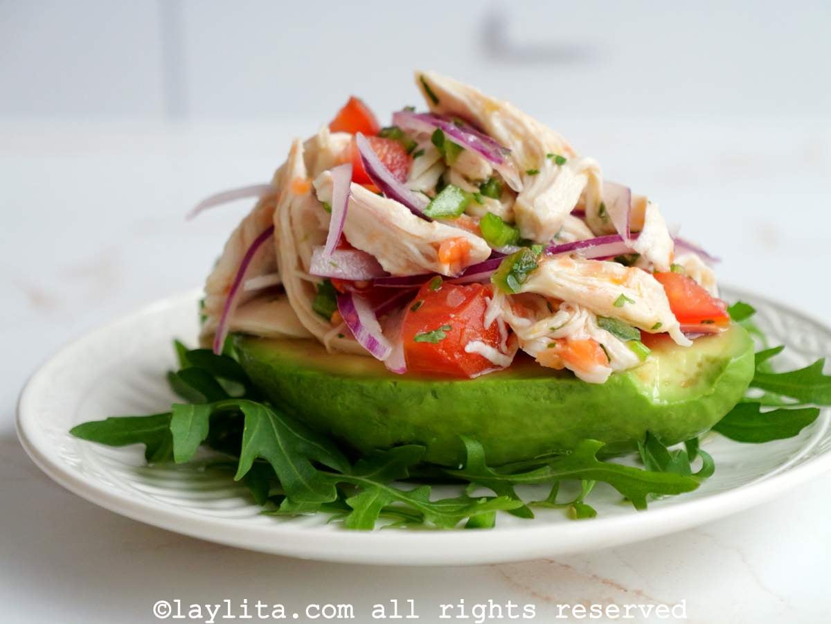 Una mitad de aguacate relleno de ceviche con pollo en un plato blanco
