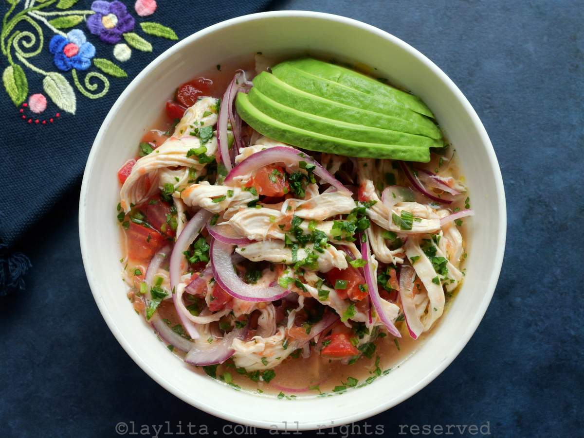 Un plato con ceviche de pollo y rodajas de aguacate en un fondo azulado