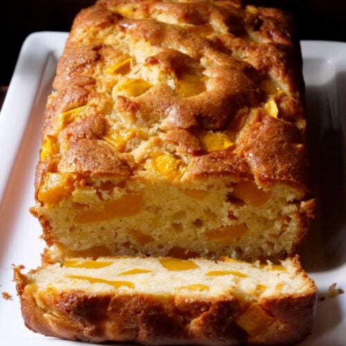 Un bizcocho de mango en un plato blanco rectangular con un pedazo del bizcocho cortado