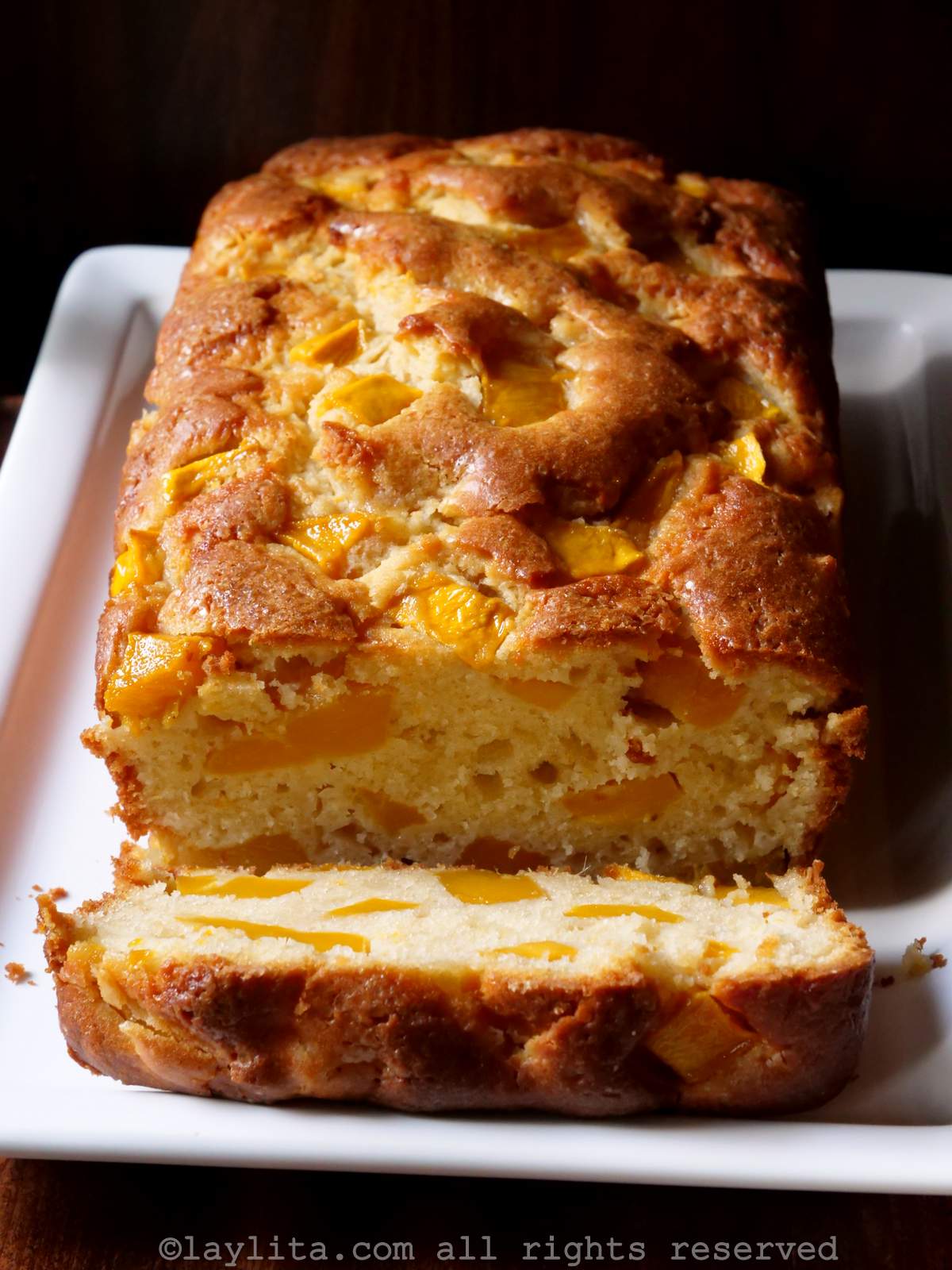 Un bizcocho de mango en un plato blanco rectangular con un pedazo del bizcocho cortado