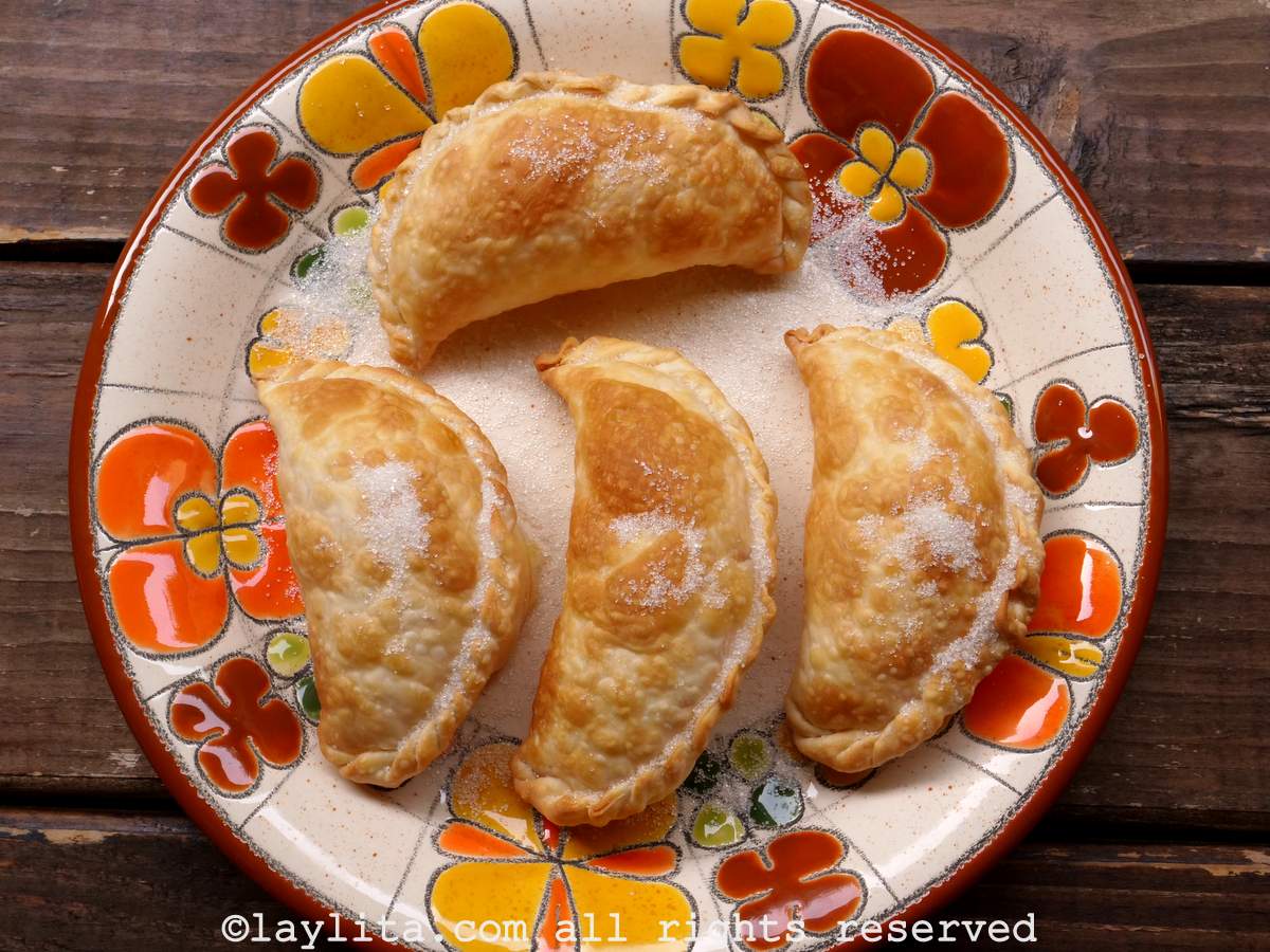 Cuatro empanadas de queso con azúcar encima en un plato con flores anaranjadas