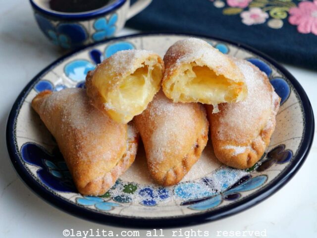 Un plato azul floreado con empanadas de queso espolvoreadas con azúcar, una de las empanadas esta cortada por la mitad