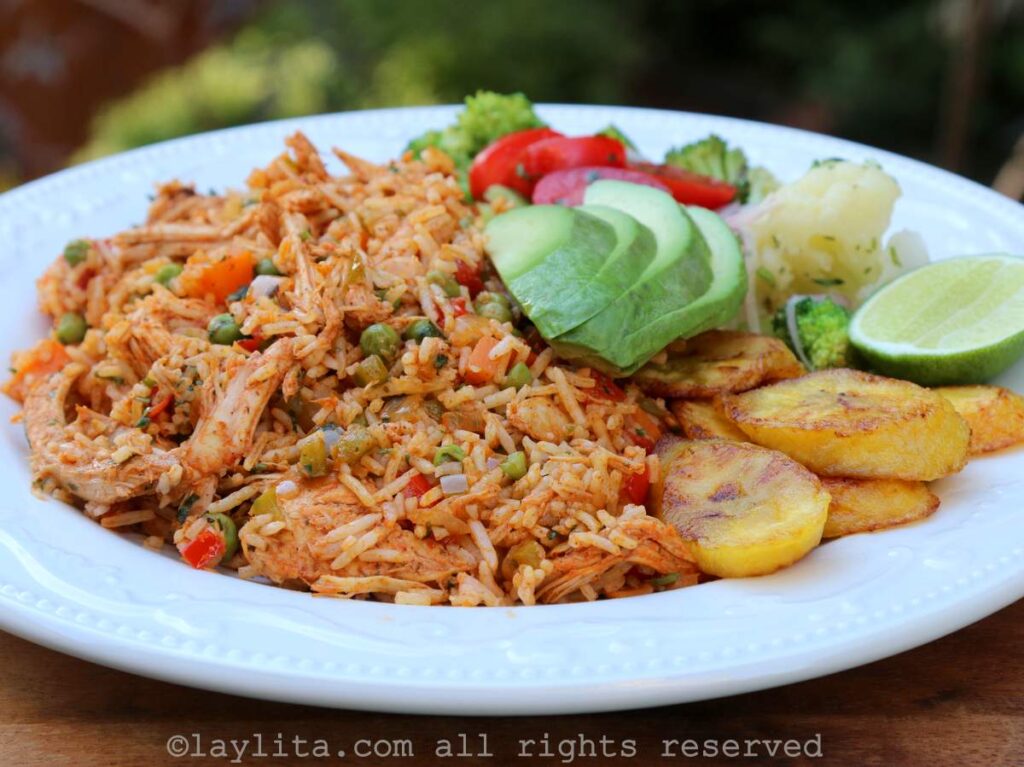 Arroz con pavo desmenuzado en un plato blanco, va acompañado con plátanos fritos, aguacate y ensalada