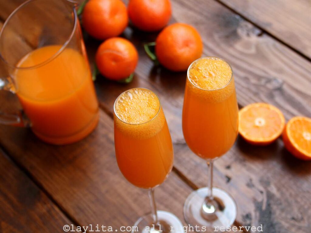 Coctel de mandarina Dos cócteles de mandarina en copas con una jarra de jugo y varias mandarinas enteras en el fondo