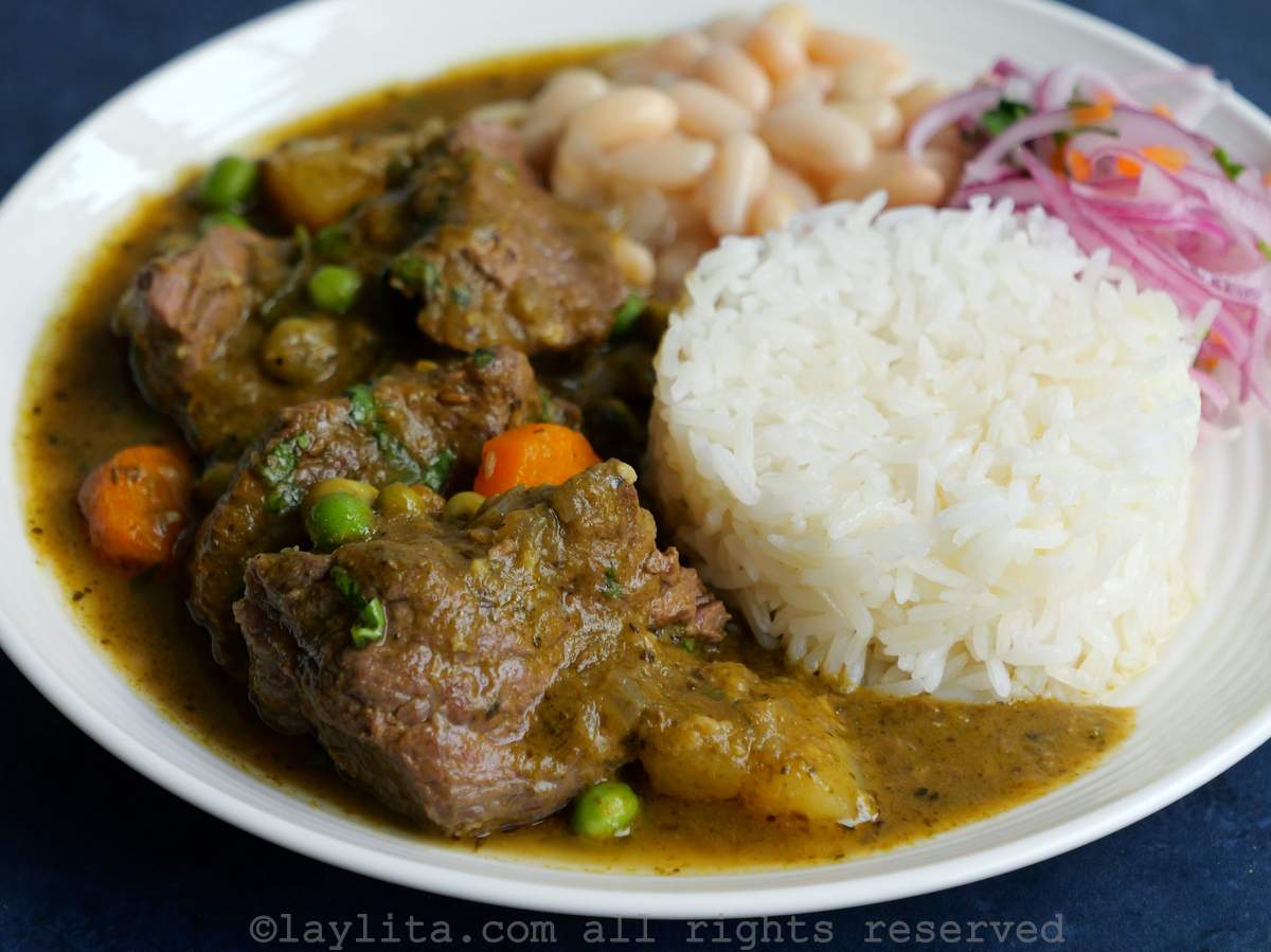 Trozos de carne guisada peruana acompañados de arroz blanco, frijoles y cebolla en un plato blanco