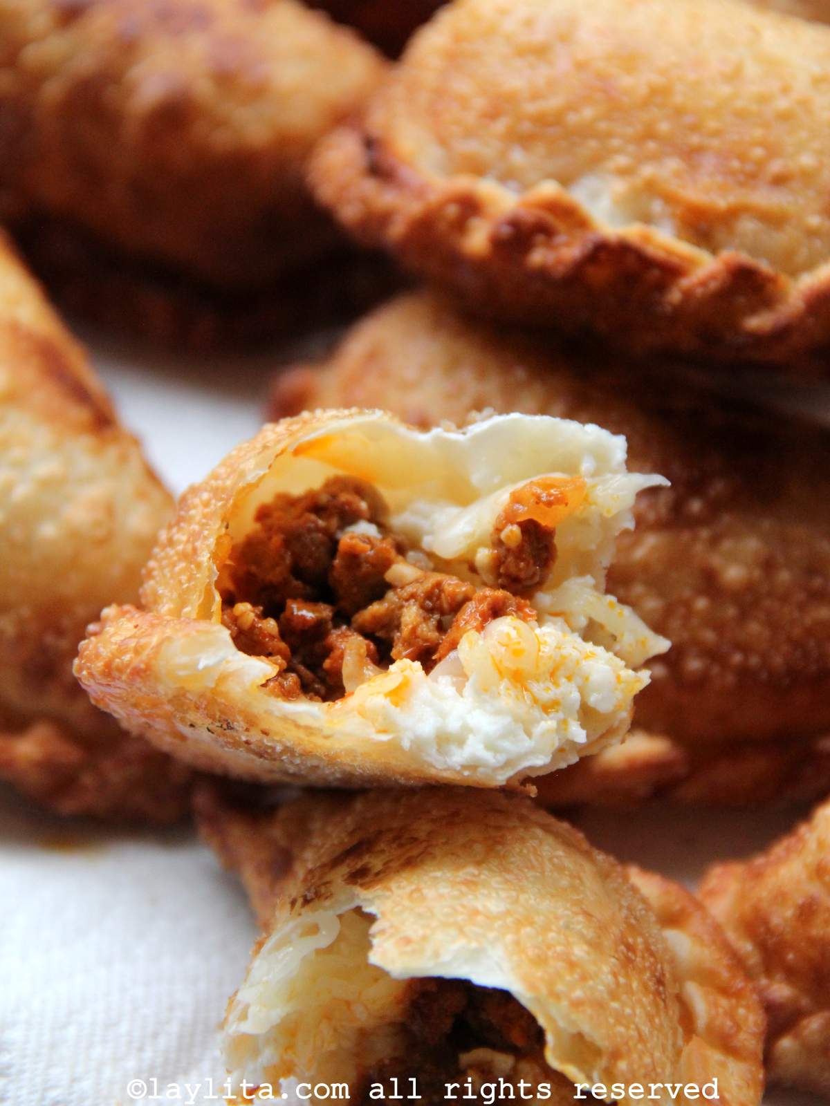 Empanadas de chorizo y queso en un plato con una empanada rota por la mitad para mostrar el relleno