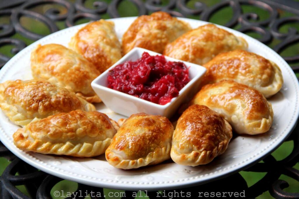 Una plato blanco lleno de empanadas de pavo con salsa de arándanos rojos en el centro