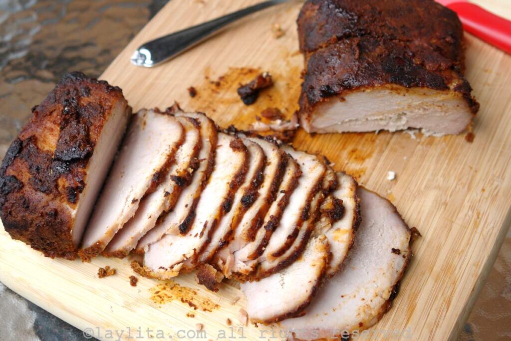 Pernil de cerdo Un lomo de cerdo asado cortado en rodajas finas en una tabla de picar