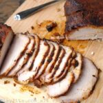 Un lomo de cerdo asado cortado en rodajas finas en una tabla de picar