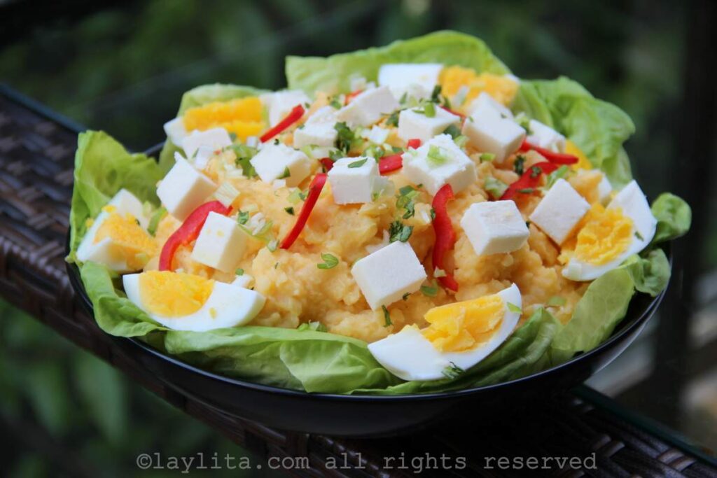 Receta del molo de papas Un plato negro con hojas de lechuga y lleno de molo de papas decorado con huevos duros, queso fresco y tiritas de ají