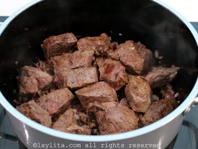 Cebolla morada picadito y ajo molido cocinandose en una olla con trozos de carne