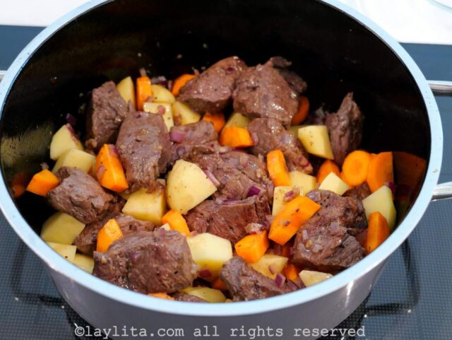 Una olla con trozos de carne, papas y zanahorias picadas