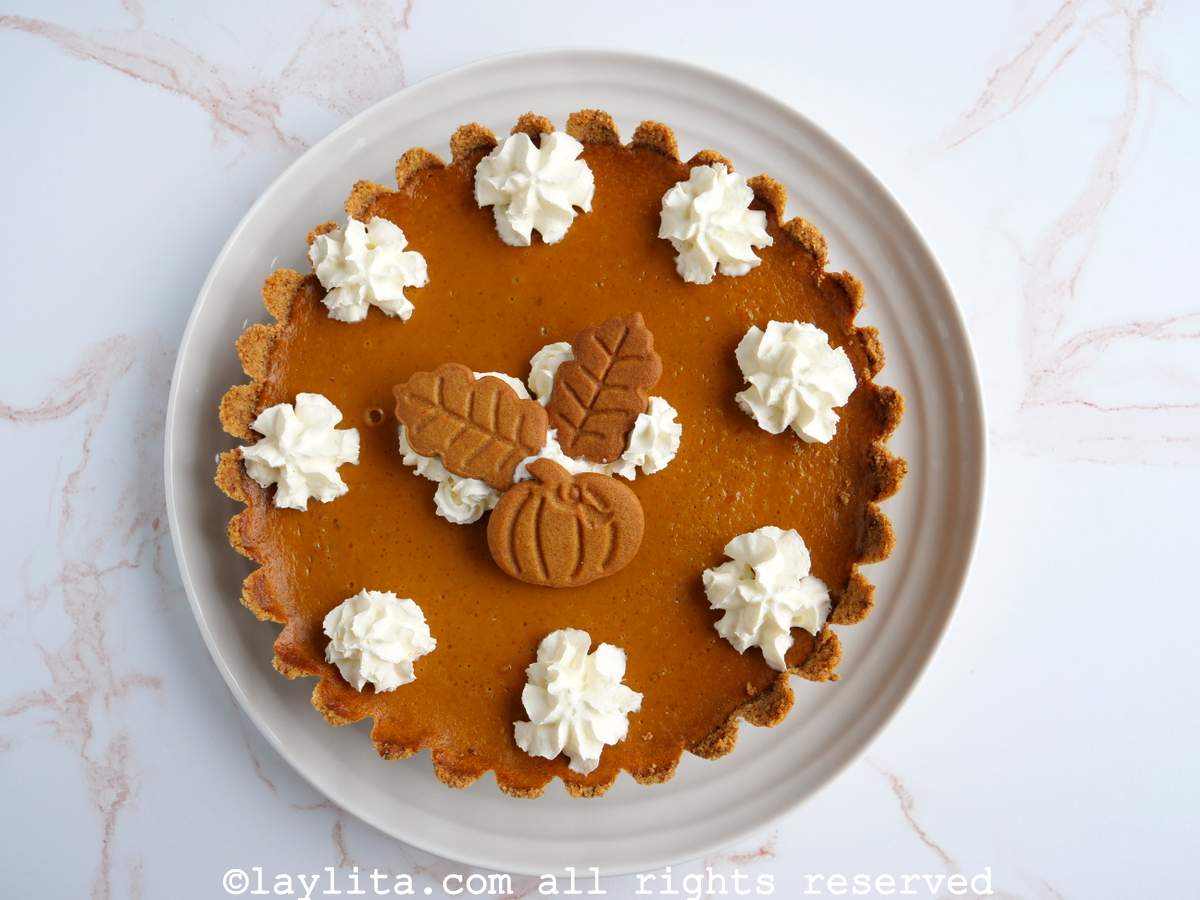 Un pay de calabaza decorado con crema chantilly y galletas en un plato blanco