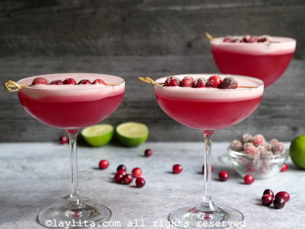 Dos cócteles pisco sour de arándano decorados con más fruta, en el fondo se ve otra copa