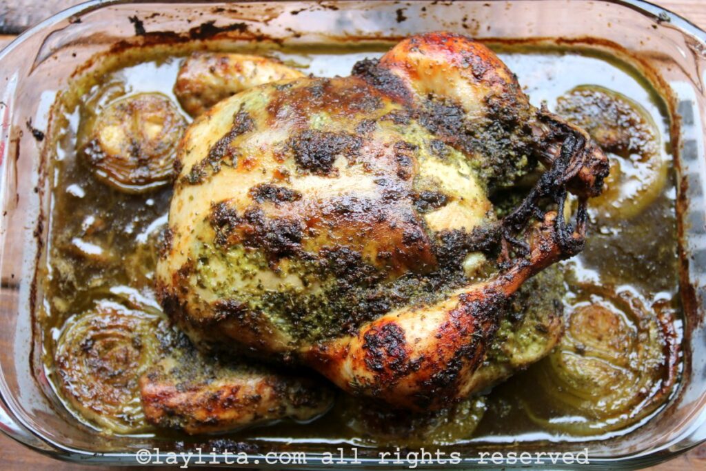 Un pollo entero asado en una bandeja con cebollas y salsa chimichurri