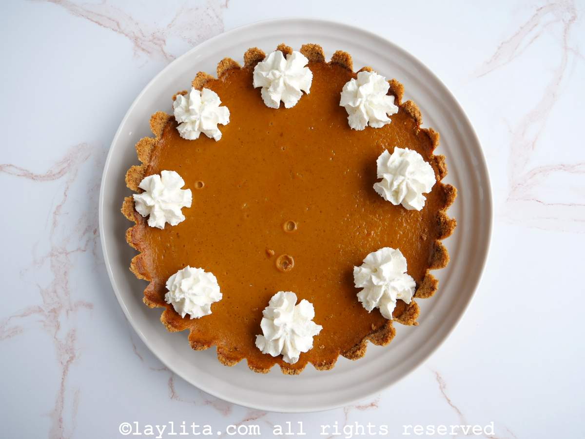 Un pie o pay de calabaza decorado con crema chantilly en un plato blanco