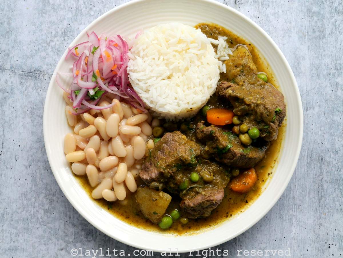 Un plato blanco lleno de seco peruano de carne, arroz, frejoles y cebolla curtida