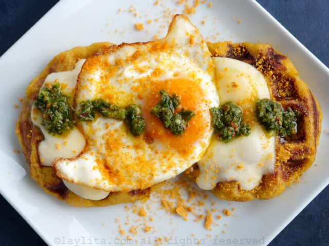 Un plato blanco con dos gofres de plátano con queso, huevo frito y chimichurri por encima