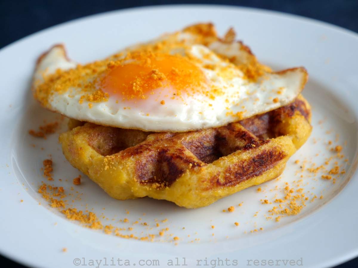 Un waffle o gofre de plátano maduro en un plato blanco con un huevo frito y sal prieta espolvoreado encima
