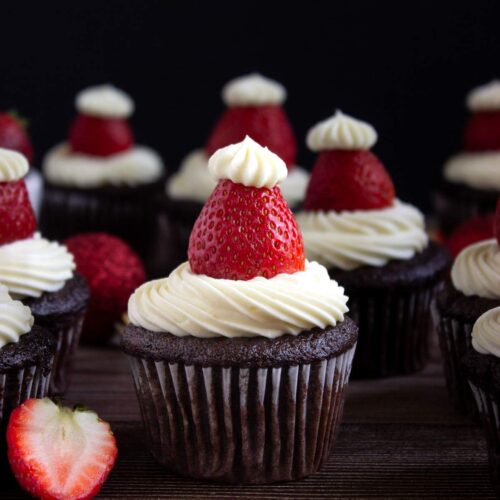 Cupcakes de chocolate decorado con ganache blanco y fresas con una fresa cortada por la mitad al lado