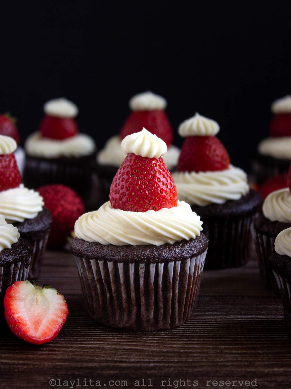 Cupcakes de chocolate decorado con ganache blanco y fresas con una fresa cortada por la mitad al lado