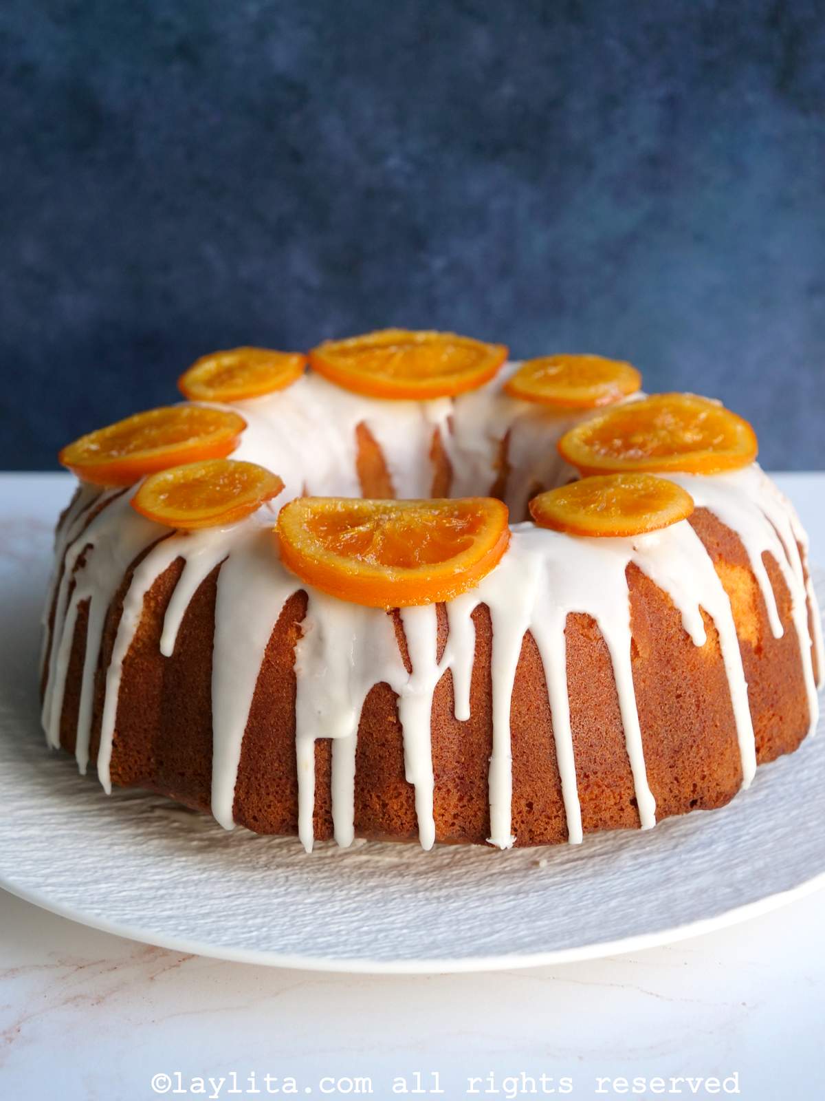 Una torta de naranja decorada con glaseado y rodajas de naranja confitadas en un plato blanco