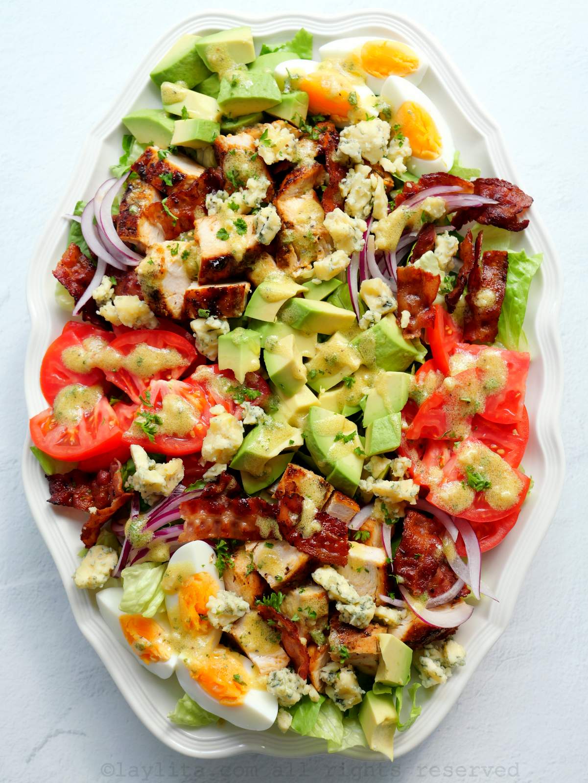 Ensalada Cobb de pollo con tocino, queso y verduras en una fuenta ovalada blanca
