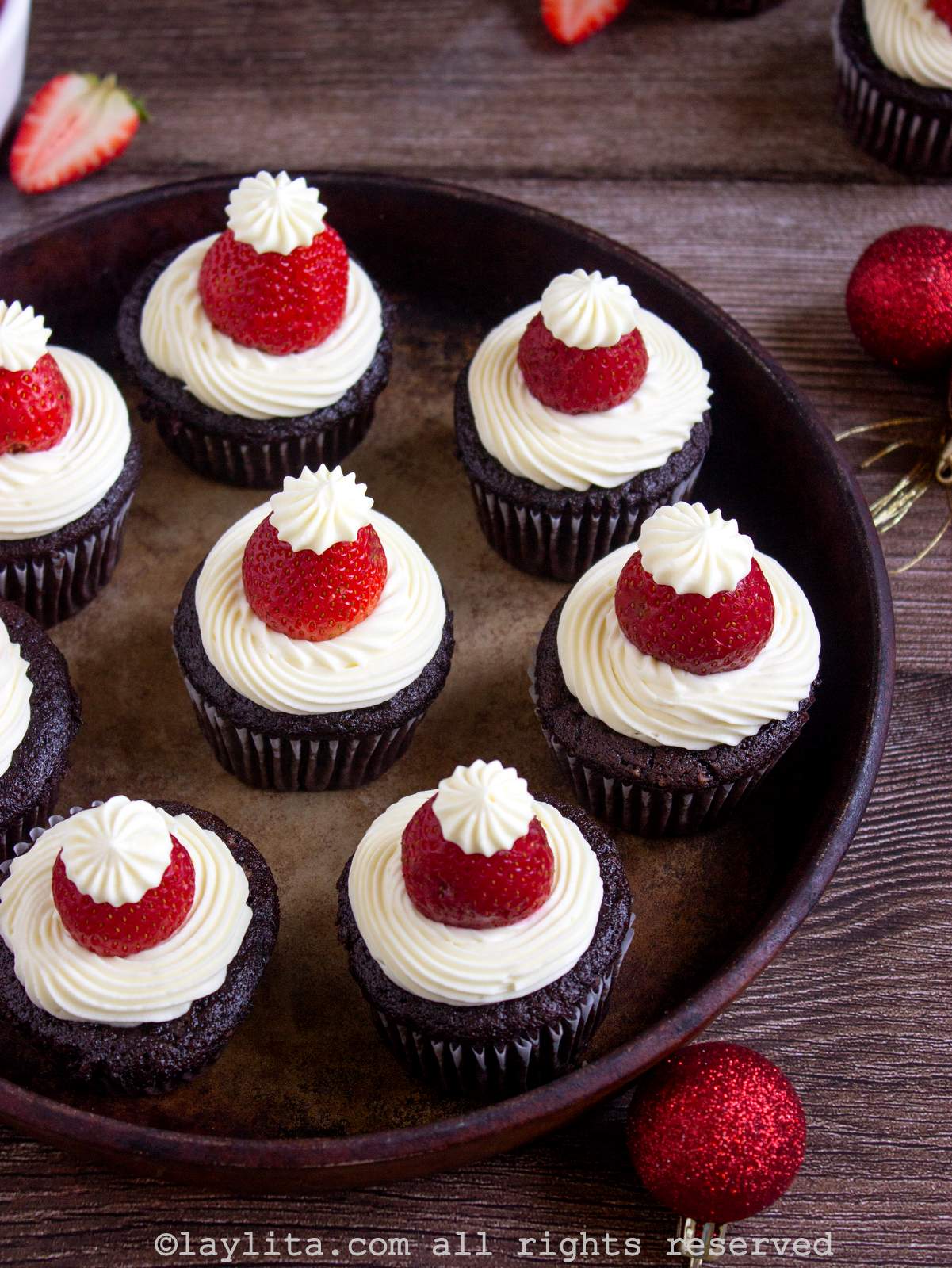 Cupcakes de chocolate con decoración navideña de Papá Noel en una bandeja encima de una mesa de madera con decoraciones navideñas al lado
