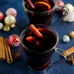 Dos vasos con vino caliente en una superficie azulada con decoraciones navideñas y especias al lado