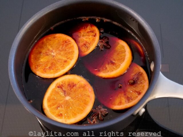 Rodajas de naranja, especias y vino tinto calentandose a fuego lento en una olla