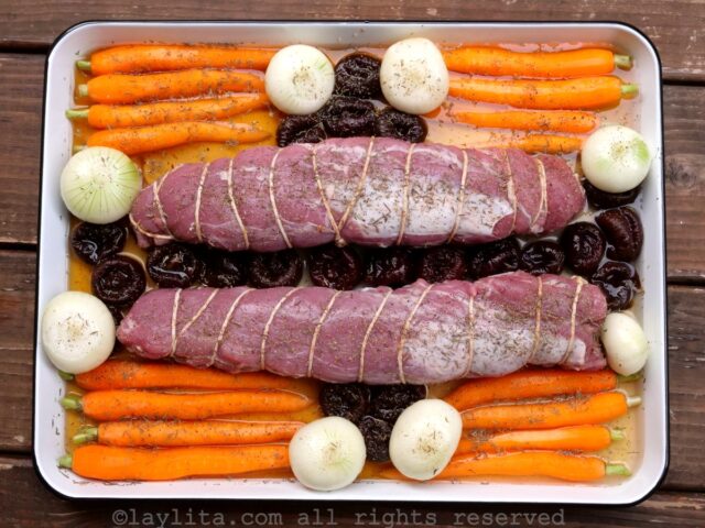 Una bandeja de hornear con zanahorias, cebollas, ciruelas pasas y solomillos de cerdo