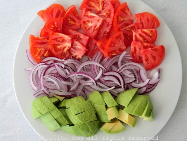 Un plato blanco con trozos de aguacate, rodajas de cebolla roja y tomates picados