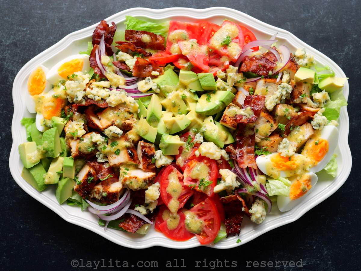 Ensalada Cobb con trozos de pollo asado, aguacate, tomate, queso, tocino, cebolla y vinagreta en una fuente blanca en una superficie negra