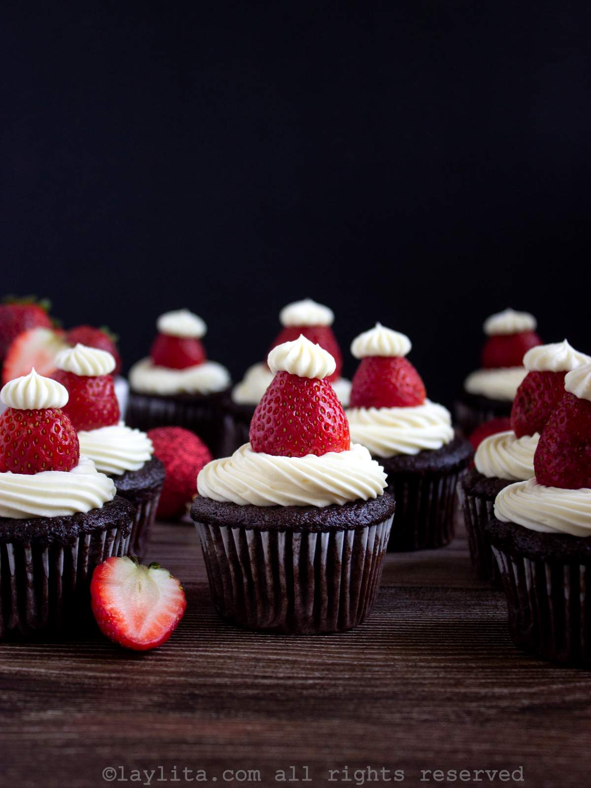 Varios cupcakes de chocolate decorados con crema blanca y fresas rojas para parecer gorros de Papá Noel
