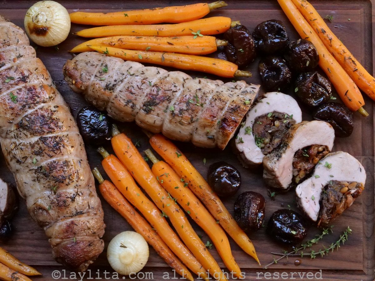 Lomos de cerdo relleno y verduras asadas en una tabla de madera, uno de los lomos tiene tres rodajas cortadas mostrando el relleno