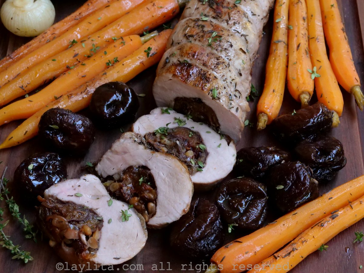 Rodajas de lomo de cerdo rellenas con ciruelas, alrededor se ven ciruelas enteras y zanahorias asadas