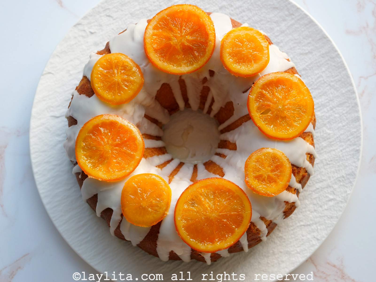 Una torta de naranja con glaseado y rodajas de naranjas caramelizadas en un plato blanco