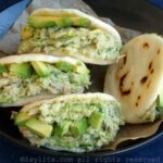 Cuatro arepas rellenas de ensalada de atún y aguacate, servidas en un bol forrado con papel pergamino.