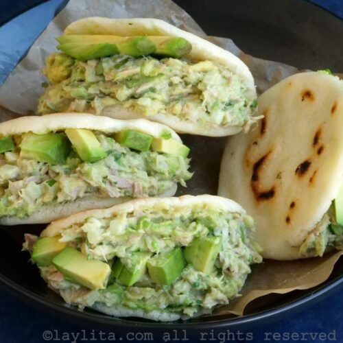 Cuatro arepas rellenas de ensalada de atún y aguacate, servidas en un bol forrado con papel pergamino.