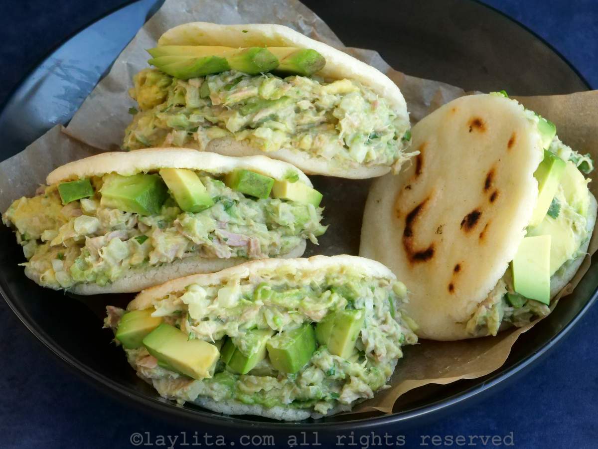 Cuatro arepas rellenas de ensalada de atún y aguacate, servidas en un bol forrado con papel pergamino.