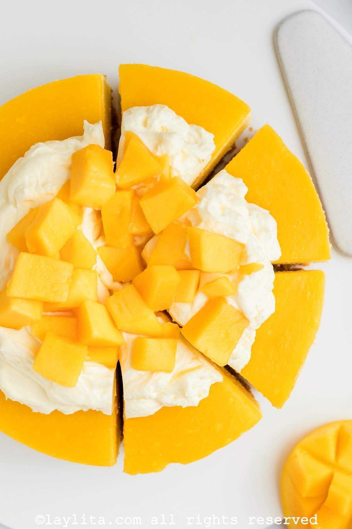 Un cheesecake de mango cortado en rebanadas y decorado con crema batida y trozos de mango