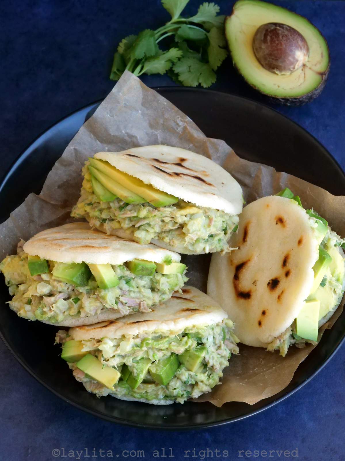 Vista superior de cuatro arepas rellenas de ensalada de atún y aguacate, servidas en un bol forrado con papel pergamino.