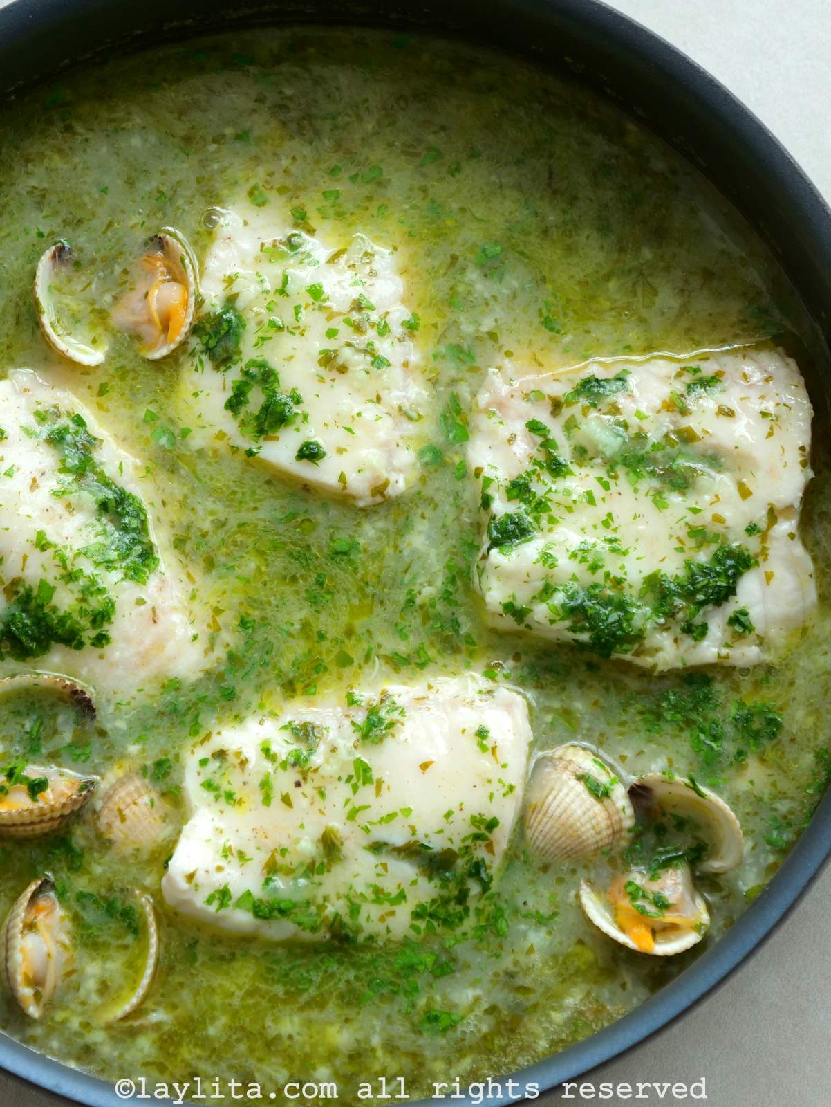 Vista desde arriba de una sartén grande llena de pescado con salsa verde y almejas