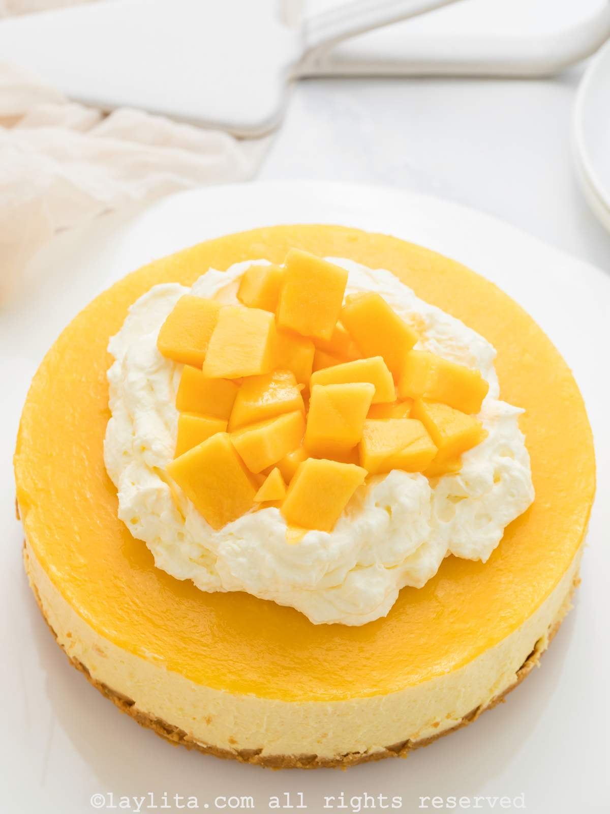 Vista superior de un cheesecake de mango decorado con crema chantilly y cubos de mango