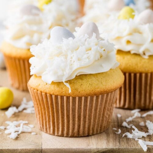 Magdalenas o cupcakes cubiertos con glaseado blanco, ralladura de coco y huevitos dulces de colores en una tabla de madera