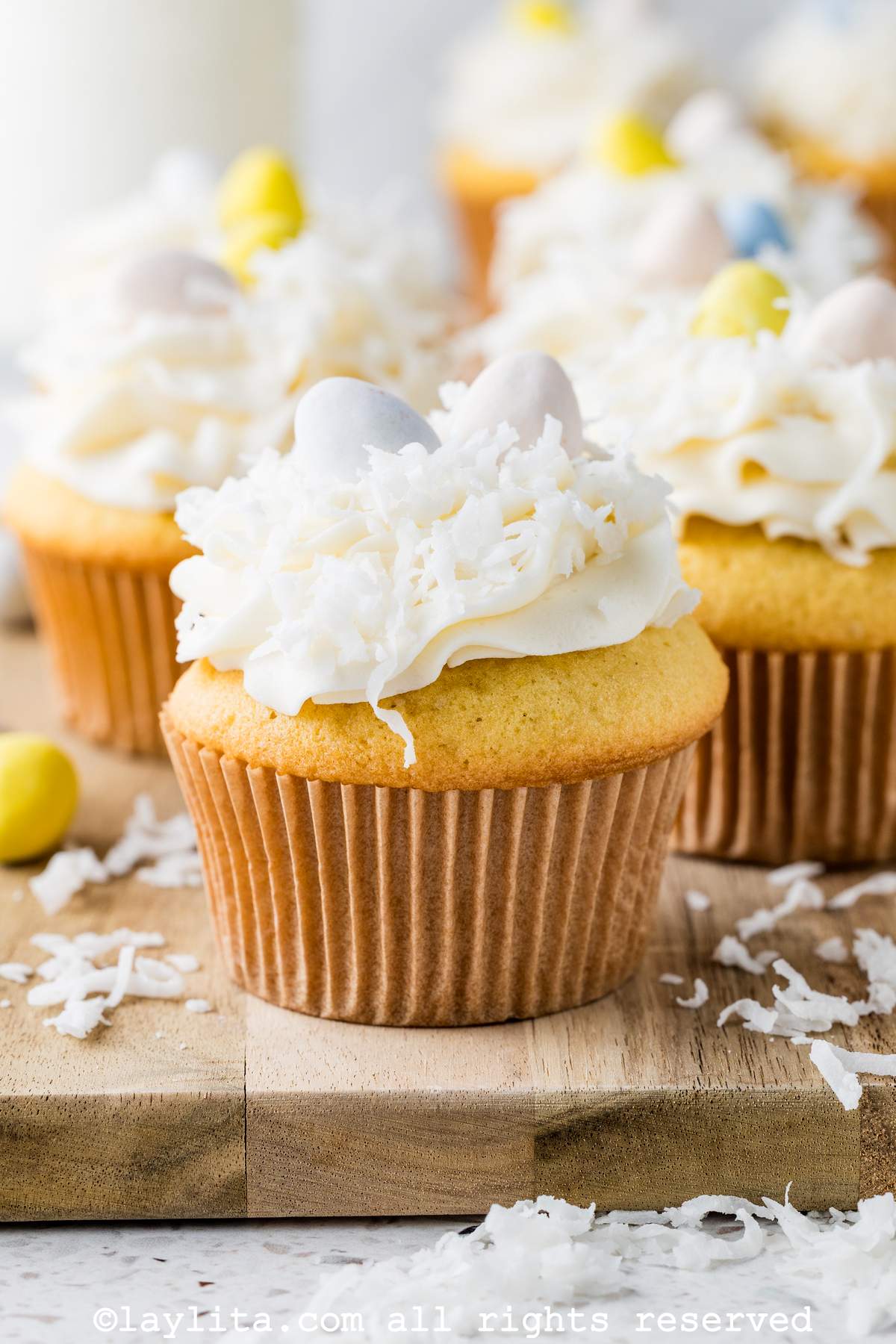 Magdalenas o cupcakes cubiertos con glaseado blanco, ralladura de coco y huevitos dulces de colores en una tabla de madera